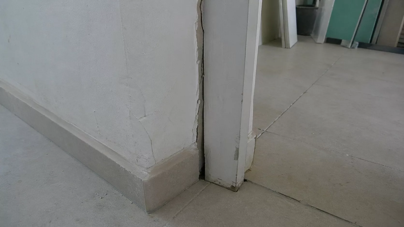 Photo réaliste d’une malfaçon de travaux dans un logement, avec fissures sur un mur intérieur, encadrement de porte abîmé, plinthes mal finies et carrelage mal aligné, illustrant les droits et recours en cas de travaux défectueux.