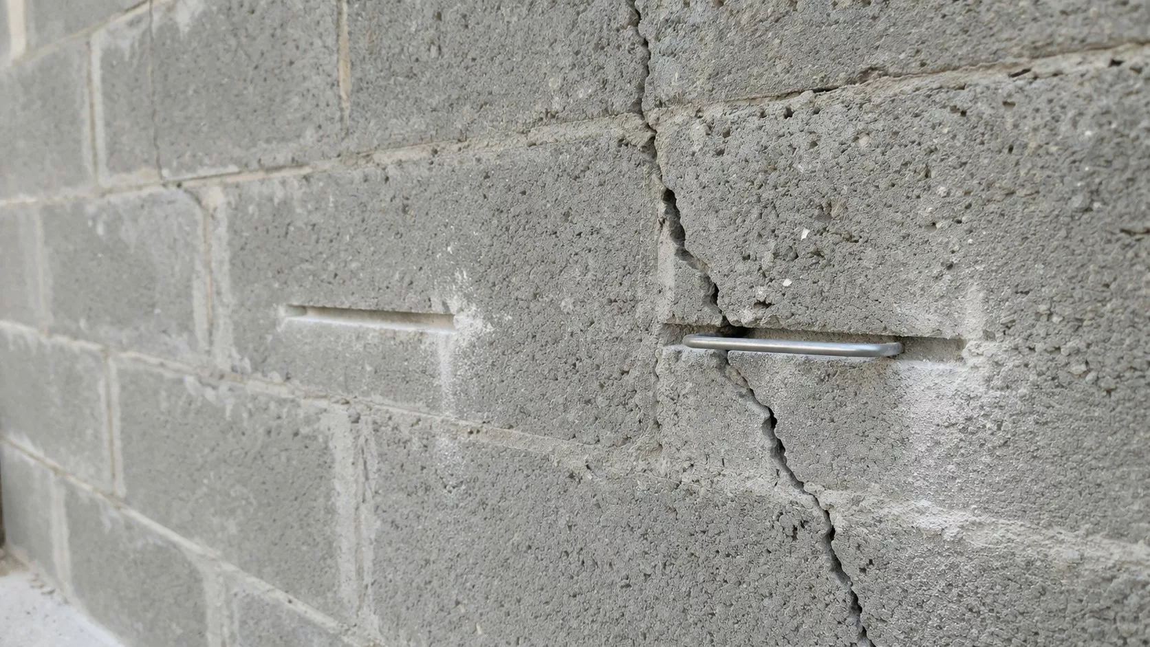 Agrafage d'une fissure sur mur en parpaing : pose d'une agrafe métallique perpendiculaire à la fissure dans une saignée réalisée à la disqueuse