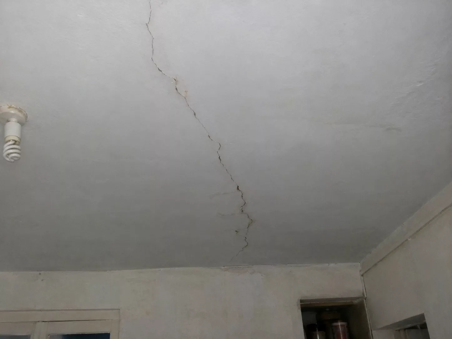 Fissure sur toute la longueur d’un plafond ancien avec traces d’usure et irrégularités du plâtre dans une pièce intérieure.