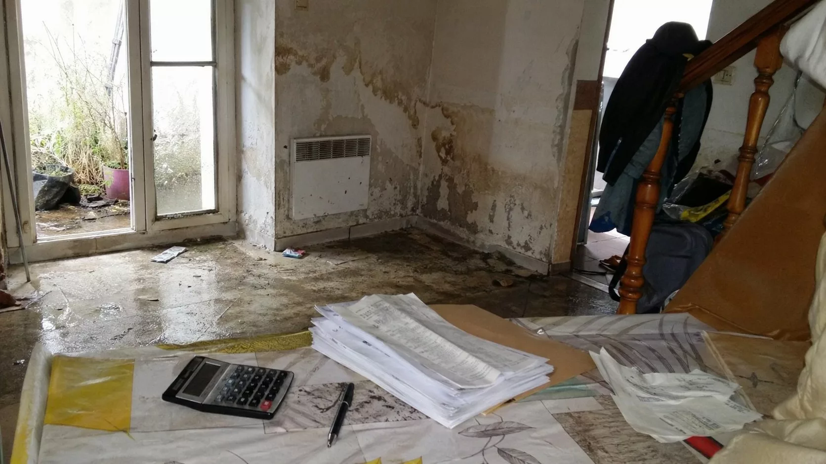 Photo documentaire d’un intérieur endommagé par une inondation avec murs humides, papiers d’assurance et calculatrice pour franchise catastrophe naturelle 2026.