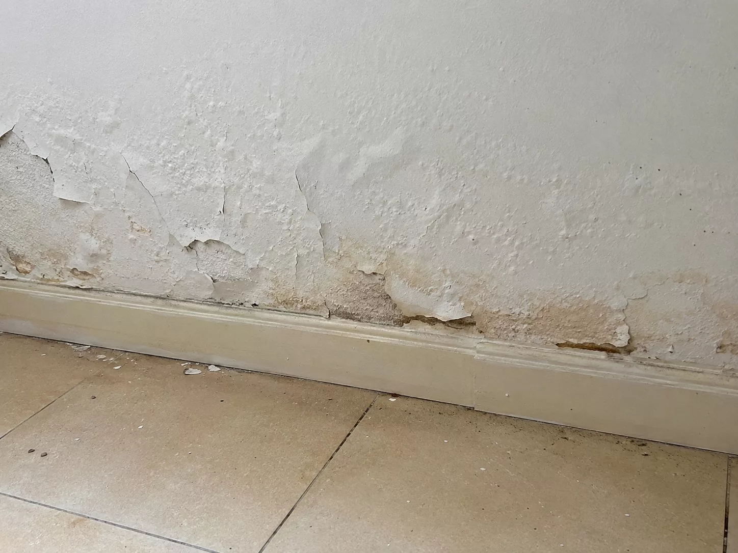 Bas de mur d'une maison ancienne avec peinture cloquée et plinthe déformée, signes typiques d'humidité ascensionnelle