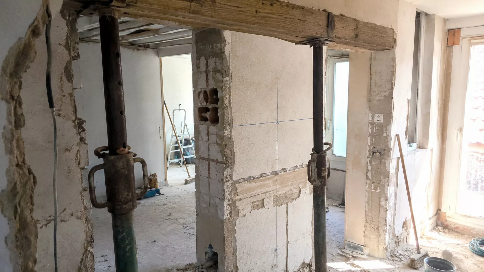 Photo documentaire réaliste au format 16/9 montrant une ouverture de mur porteur en rénovation intérieure avec étais métalliques, poutre provisoire en bois, maçonnerie apparente, poussière de chantier et vérification de la structure avant travaux, 26 juin 2026.