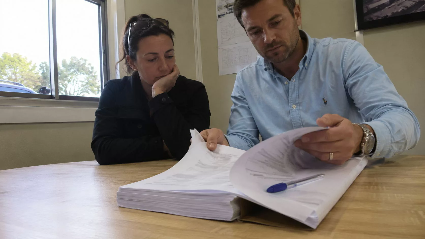 Couple d'acquéreurs lisant attentivement des documents contractuels avant de signer, préparation d'un achat immobilier sécurisé par une expertise avant achat