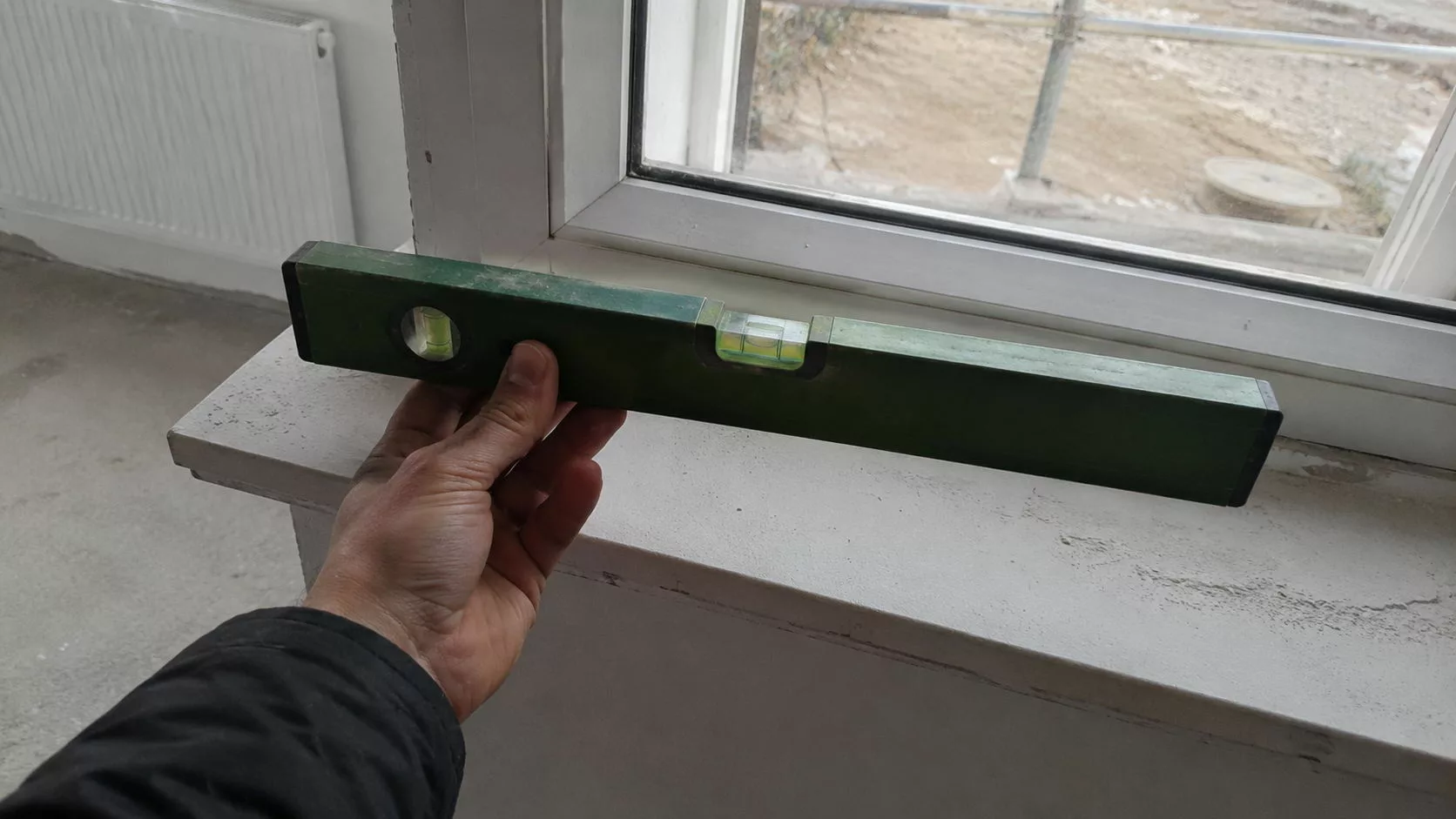 Contrôle de l'horizontalité d'un appui de fenêtre au niveau à bulle sur un chantier, vérification technique lors d'une expertise bâtiment avant achat en Île-de-France