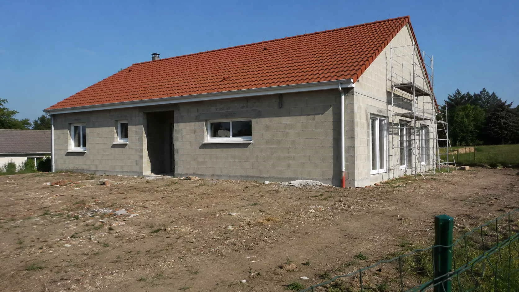 Maison individuelle récente en cours de gros oeuvre, murs en parpaings et charpente, sur un terrain de construction en Île-de-France