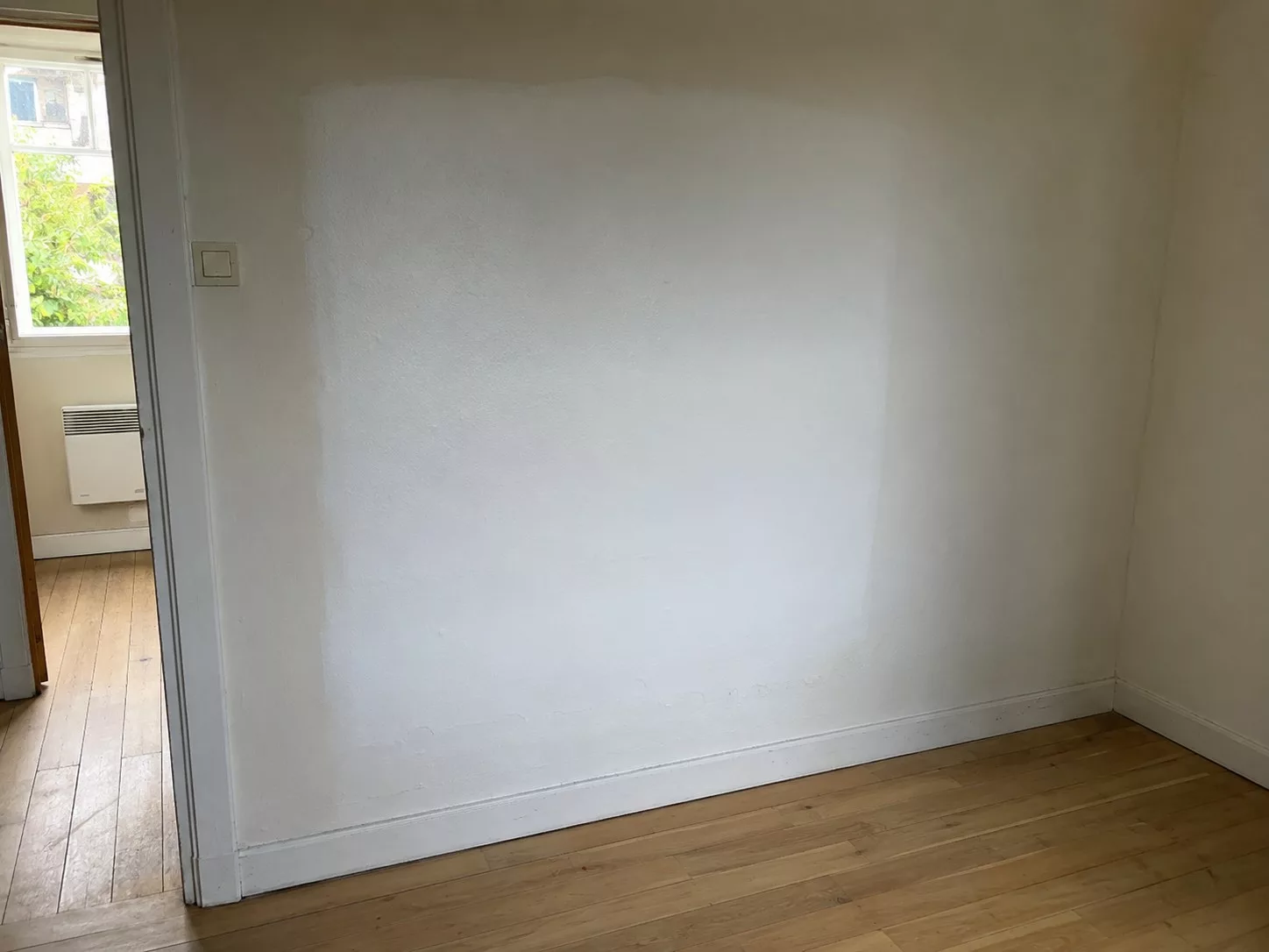Mur intérieur d'une maison à vendre avec zone repeinte plus blanche près de la plinthe masquant fissure et humidité. Score Expertises, expert bâtiment Paris et Île-de-France.