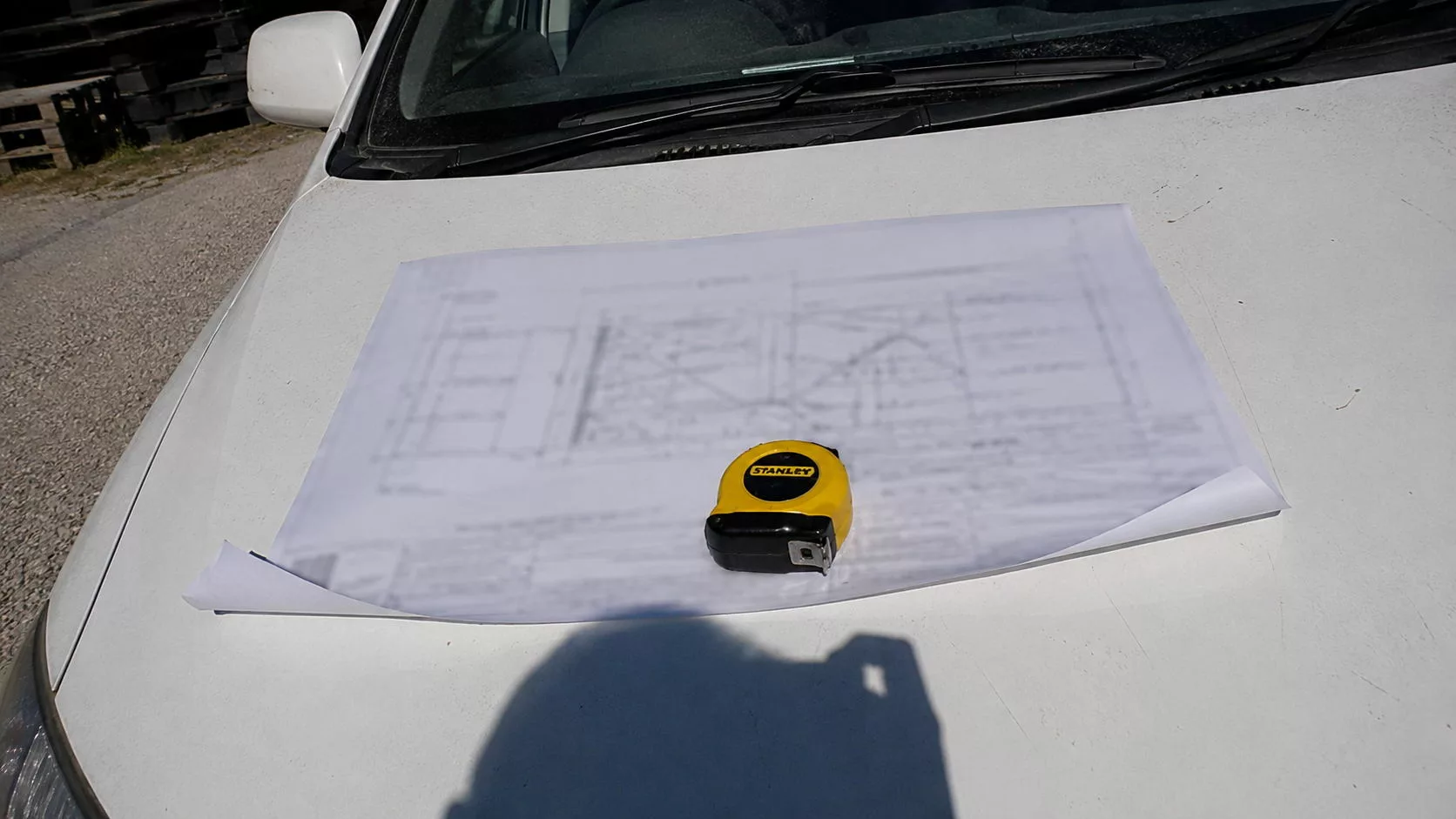 Plan d'architecte déplié sur un chantier de maison individuelle avec mètre ruban, lors d'une visite de pré-réception, expertise bâtiment Score Expertises Île-de-France