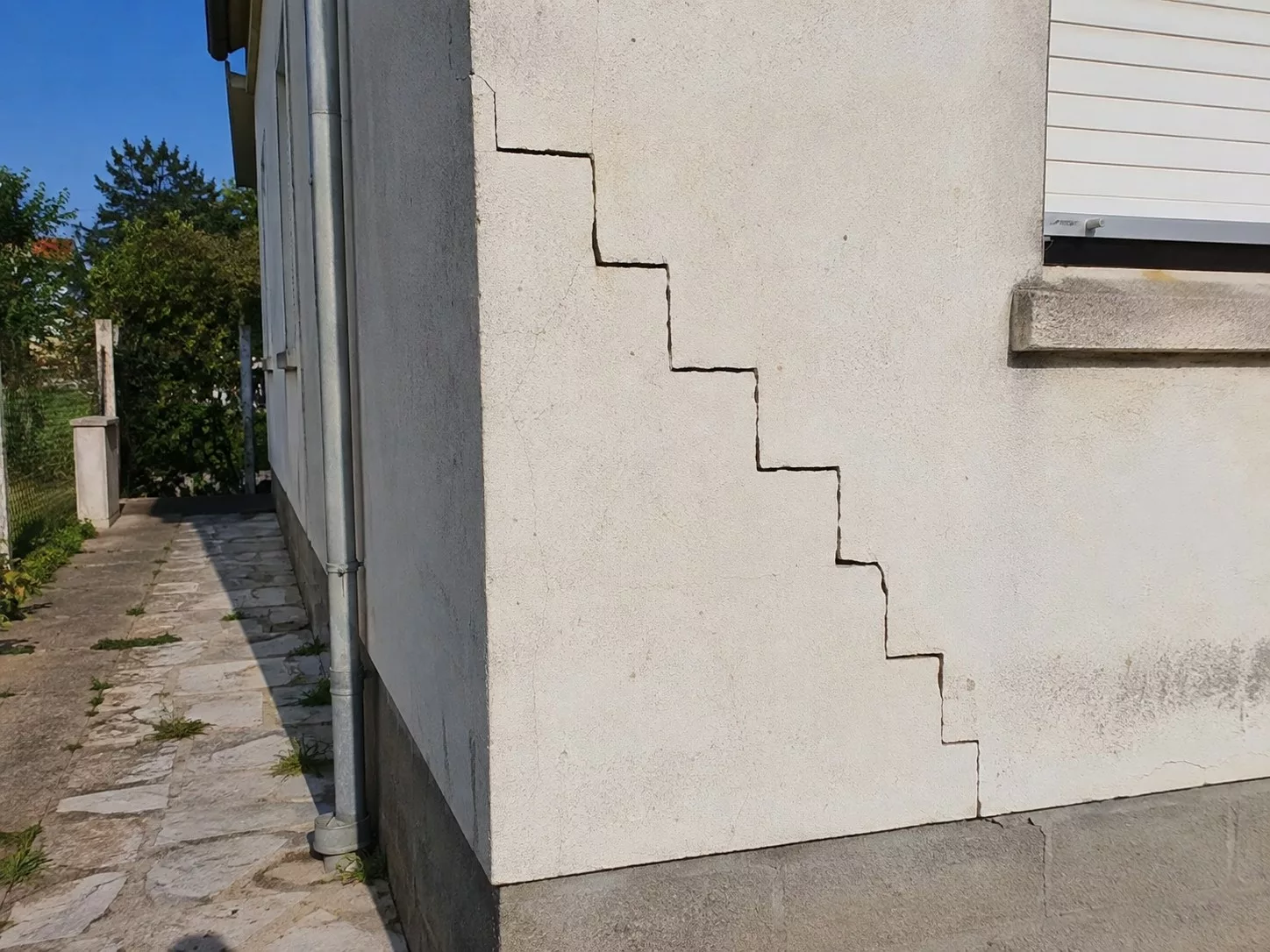 Fissure en escalier sur la façade enduite d'un bâtiment, à l'angle d'un mur
