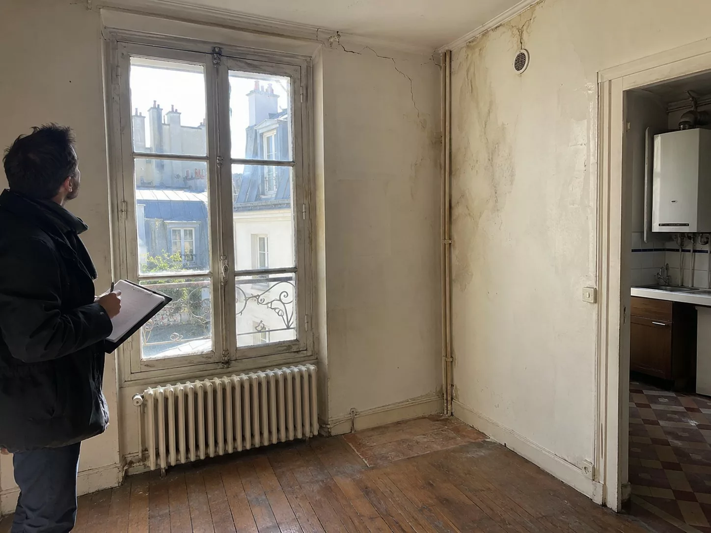 Expertise avant achat d’un appartement ancien, inspecteur avec clipboard face à une grande fenêtre bois dégradée